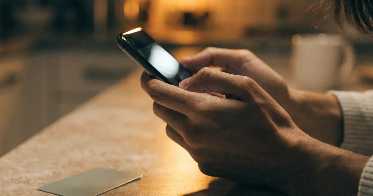Hands holding a phone with a debit card on the counter — cash app fee calculator for instant deposit fees