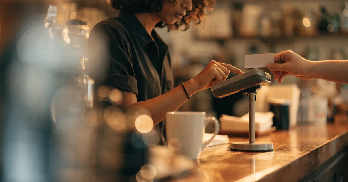 Card terminal on a coffee shop counter being tapped — square fee calculator for processing fees and net deposit