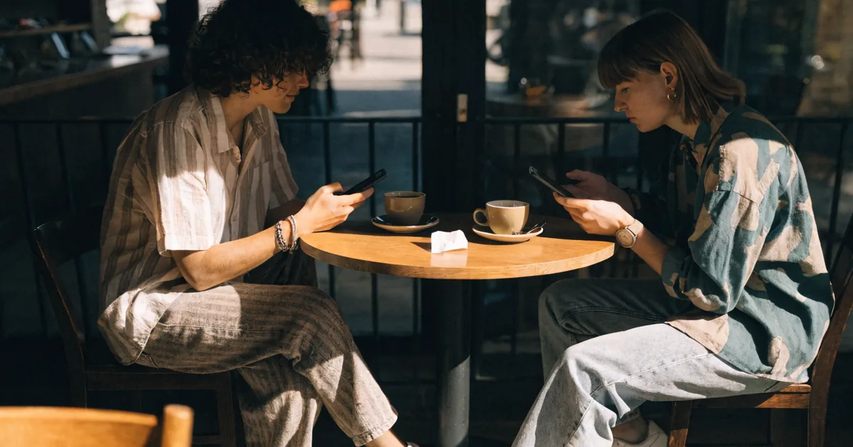 Two friends splitting a bill with phones at a cafe — venmo fee calculator for instant transfer and seller fees